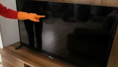 Pers wijst naar zwart scherm van flatscreen televisie op houten meubel.