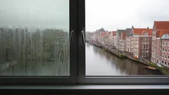 Uitzicht op Amsterdamse grachten vanaf beslagen raam, met karakteristieke huizenrij.