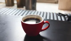 Rode koffiekop op een zwarte tafel, vers gezette koffie, ochtendlicht, gezellige sfeer