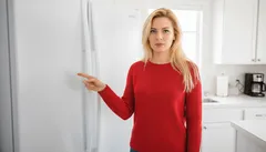 Vrouw in rode trui wijst naar koelkast in moderne witte keuken