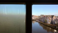 Uitzicht op Nederlandse grachten en huizen door beslagen treinraam