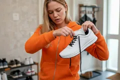 Vrouw in oranje trui strikt witte sneaker in moderne kamer met schoenenrek op achtergrond.