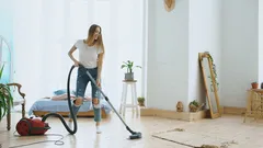 Jonge vrouw danst en zingt tijdens het stofzuigen van een moderne woonkamer