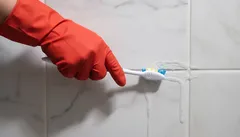 Tegels schoonmaken met tandenborstel en rode schoonmaakhandschoen
